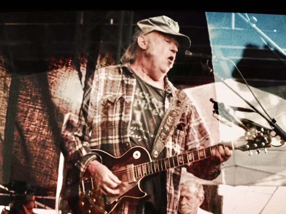 Grainy photograph of Neil Young holding a guitar and singing into a microphone.