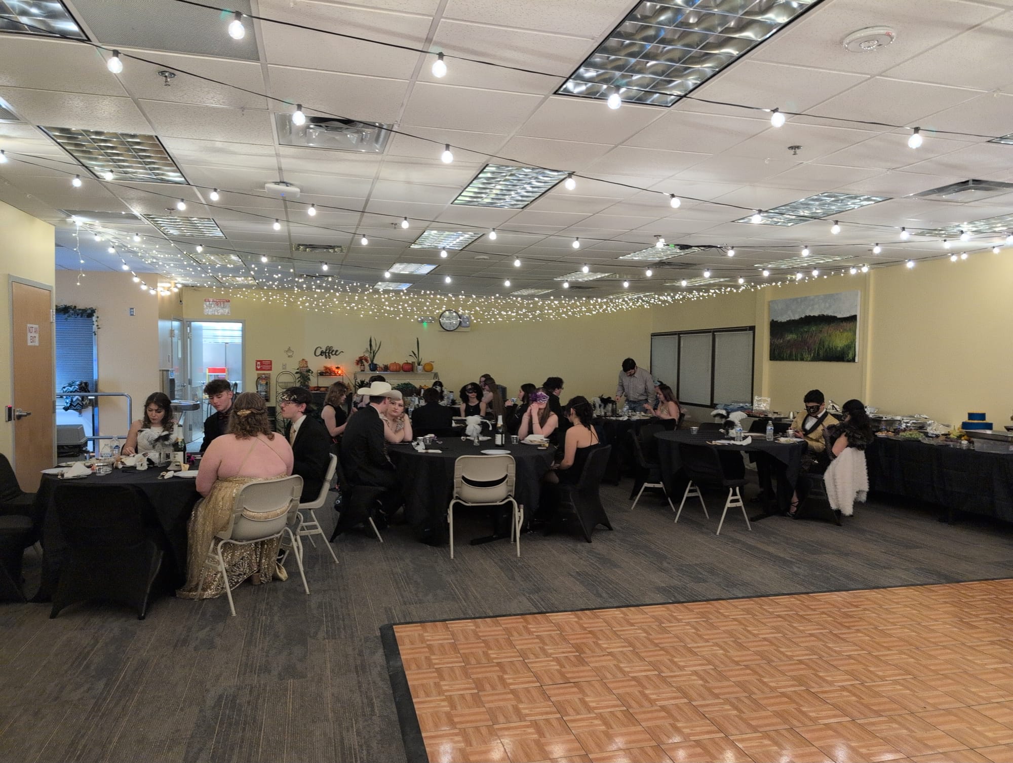 About 30 students in formal attire seated at tables in the cafeteria.