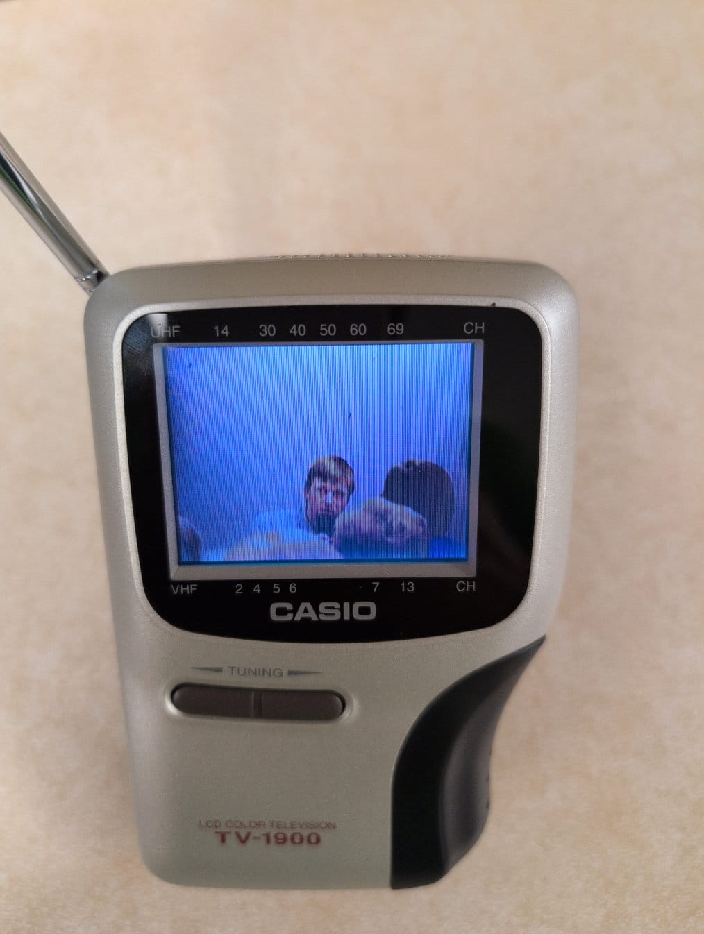 A small handheld TV displays an image of an intellectual speaking to an audience.