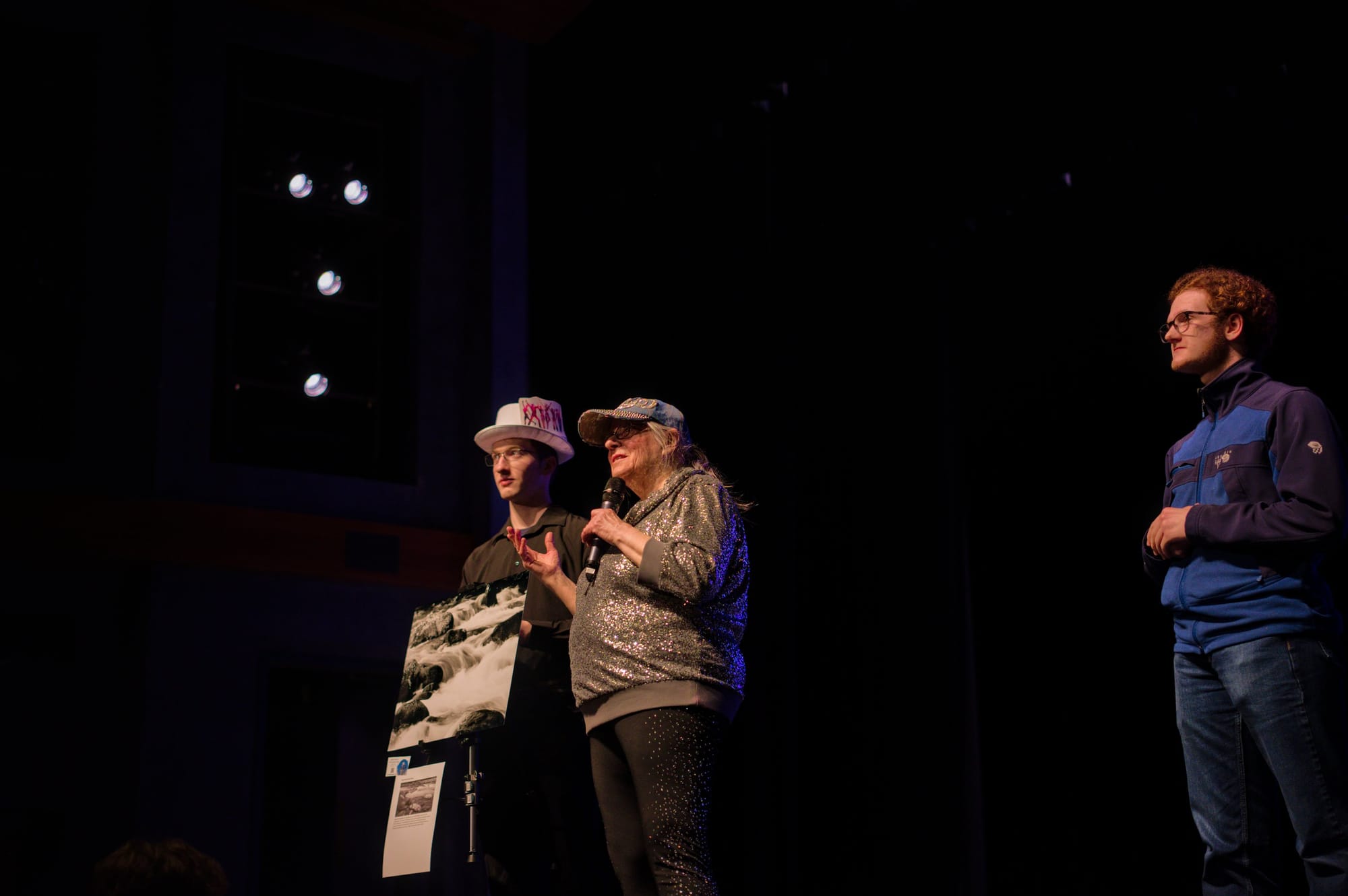 Three people stand on stage, looking out at the audience.