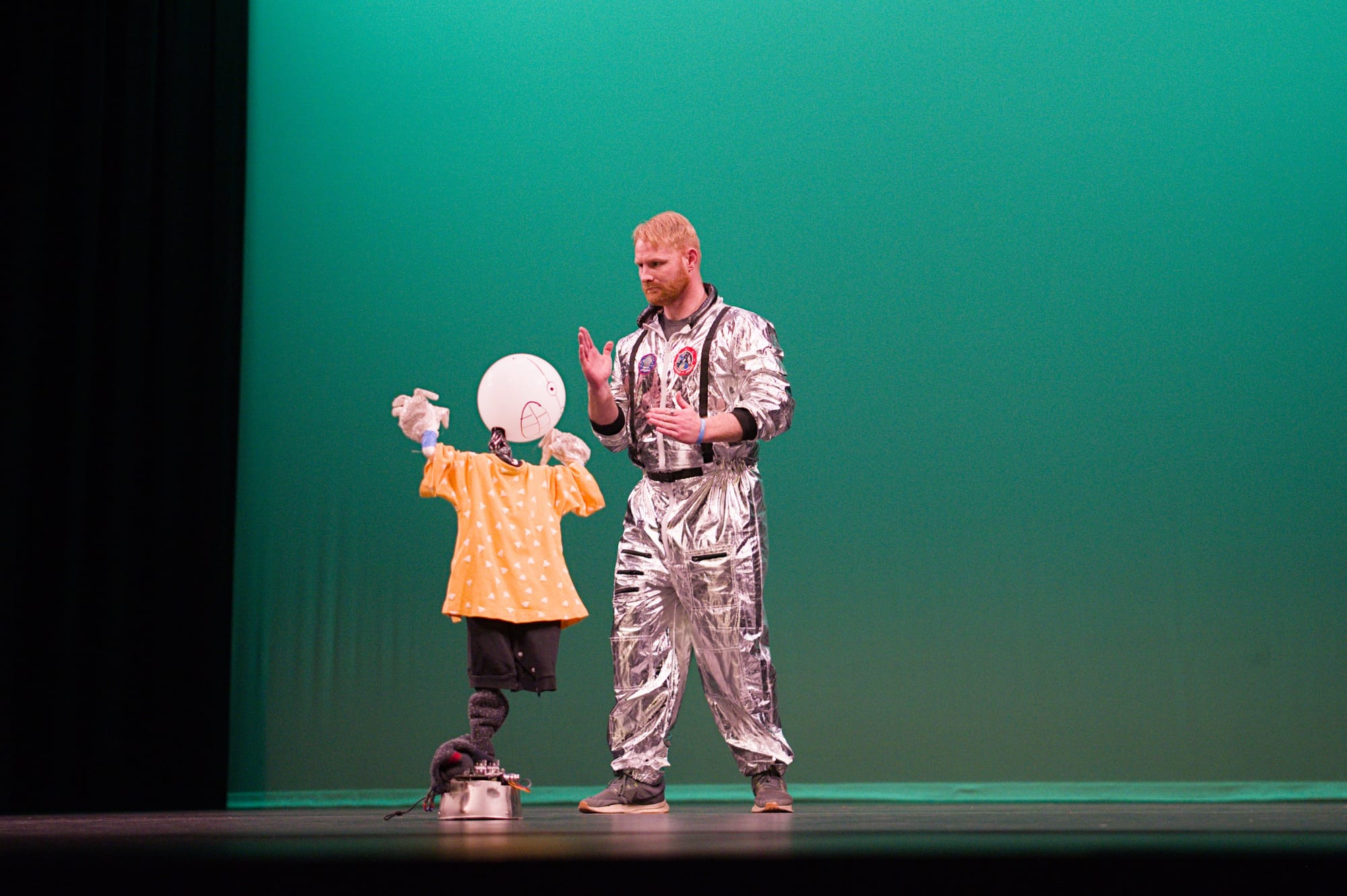 A primitive stationary robot with a balloon for a head and a man in a silver "space suit." Both are dancing.