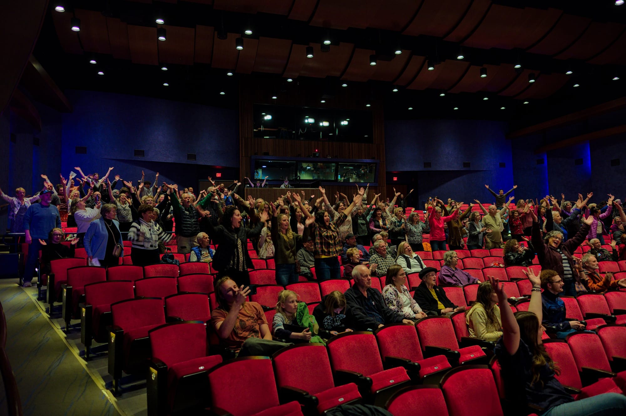 A wide shot of the audience of about 150 people, many of them performing movements with their arms.