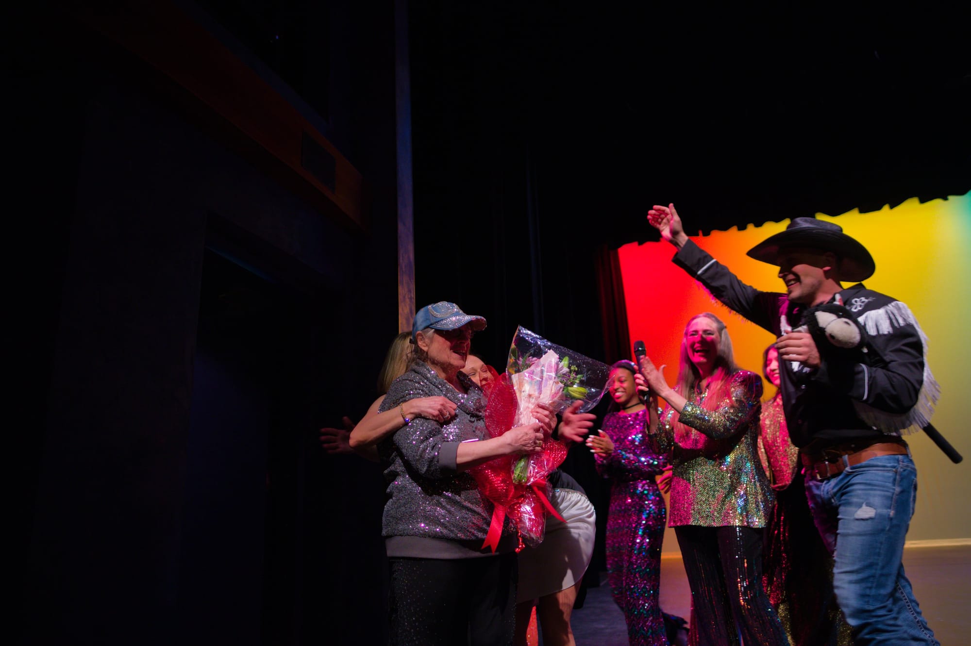 Students in costumes approach and hug a woman at the edge of the stage.