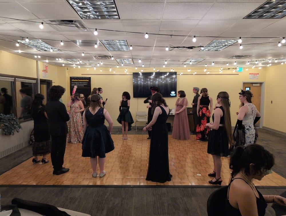 16 students dressed formally, with masks, standing on a portable dance floor.
