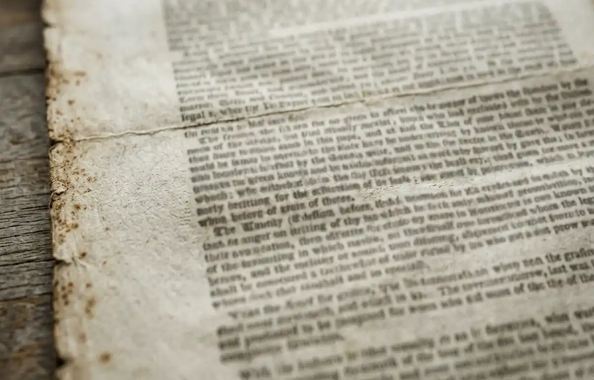A close-up of an aged legal document page in soft light, with dense typeset paragraphs blurred and unreadable. No words, seals or signatures are legible.