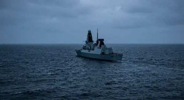 A modern naval vessel at sea, photographed in cold blue-grey light against open water. No human figures visible. The vessel is angled away from the viewer