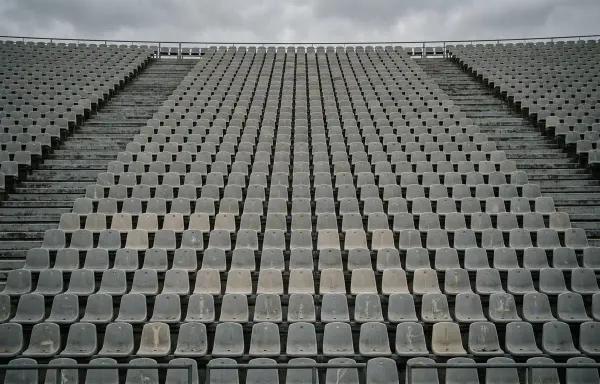 A vast stand of empty stadium seats filling the frame in flat overcast light, muted grey and pale tones. No people, signage or text are visible.