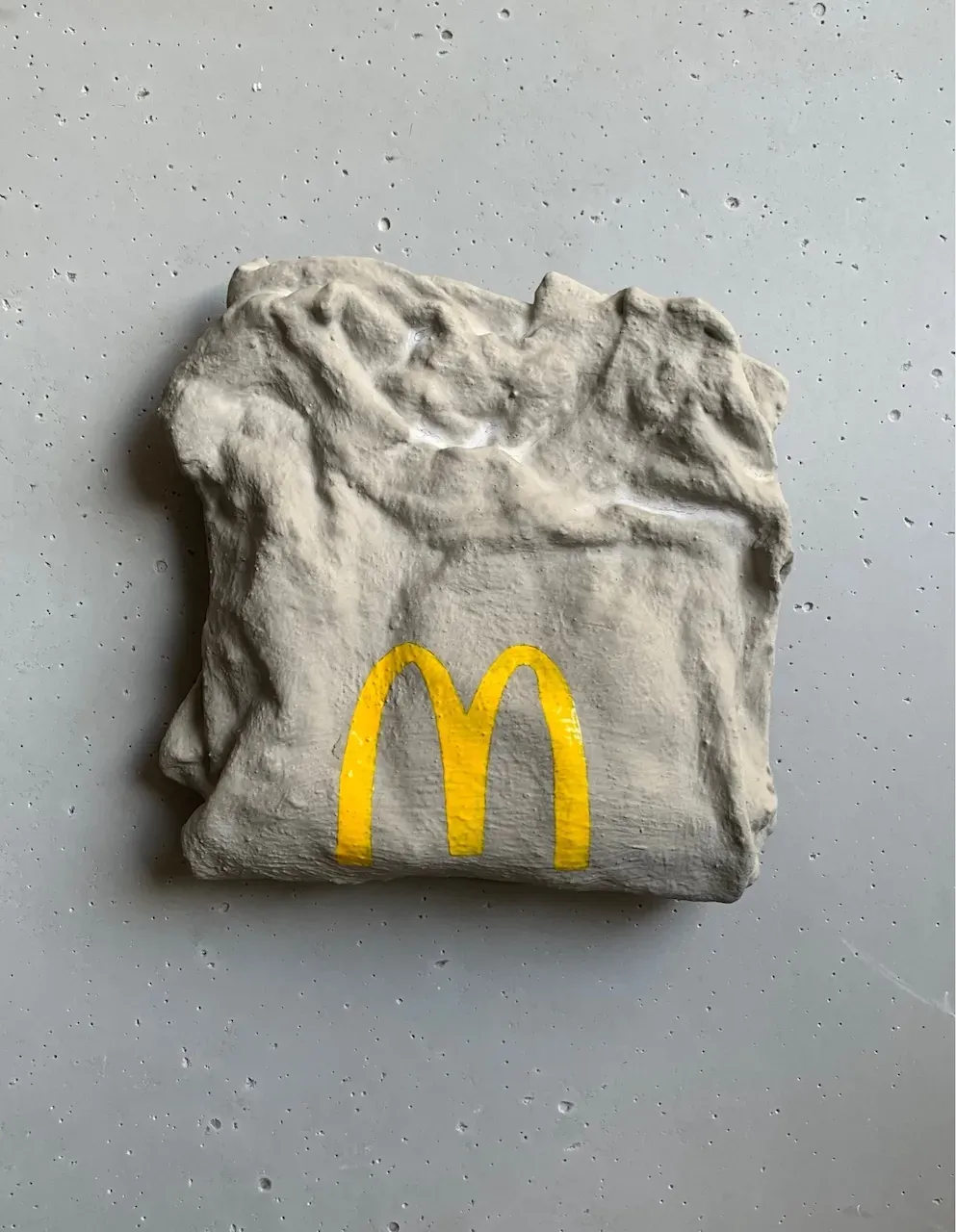 Photo of a ceramic sculpture of a folded grey t-shirt with the McDonalds logo on it.