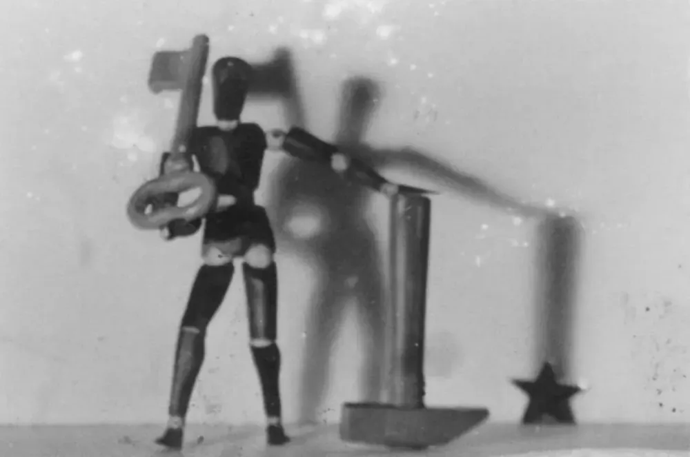 vintage grainy photo of a small wooden human figure holding a large key and standing next to a large inverted hammer