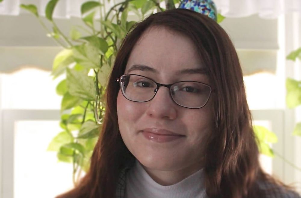 Hazel wearing a blazer smiling with a background of plants.