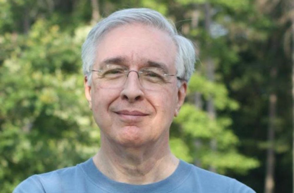 Photo of an older white guy with short grey hair and rimless glasses with a bemused smile.
