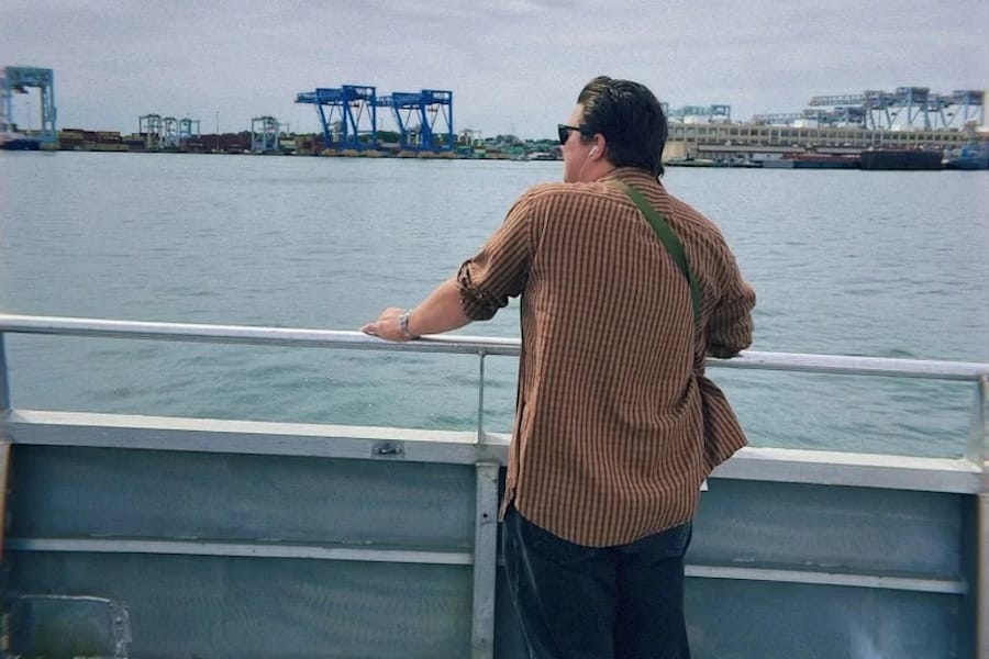 Man wearing orange shirt standing on boat overlooking harbor.