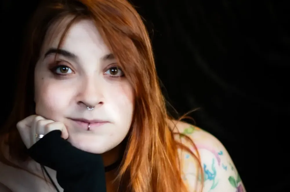 Person with long red hair and tattoos.