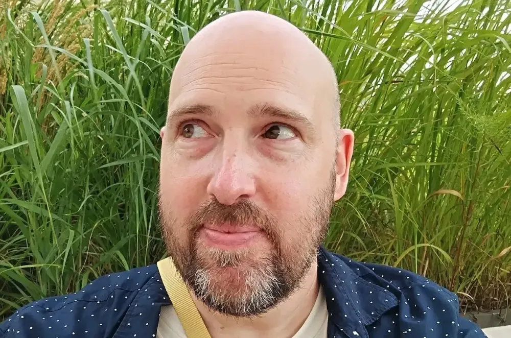 Bald male who looks 30 to 40 years old, with brown eyes and a short graying beard. His eyes are looking up and to his right, away from the viewer.