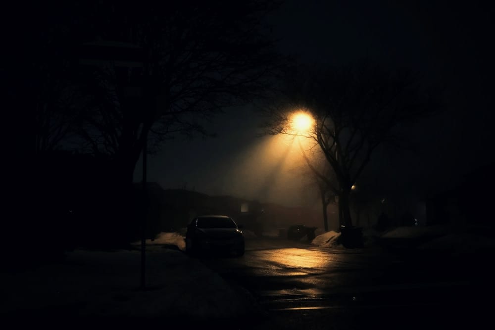 A streetlamp illuminates a foggy, wet street at night