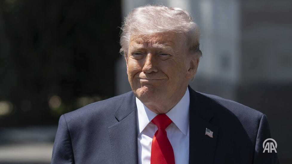 Close-up photo of Donald Trump in a dark suit, white shirt, and red tie with an American flag pin.