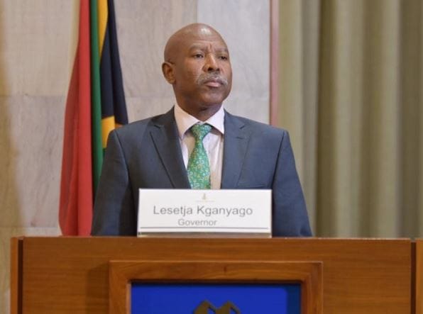 Lesetja Kganyago in a suit standing behind a wooden podium with a nameplate reading 'Lesetja Kganyago Governor'.