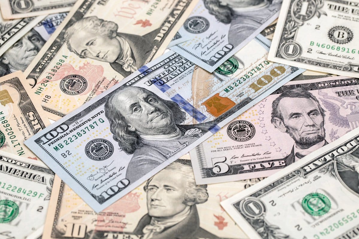 Close-up of scattered United States dollar bills including $100 notes with Benjamin Franklin and $5 notes with Abraham Lincoln.