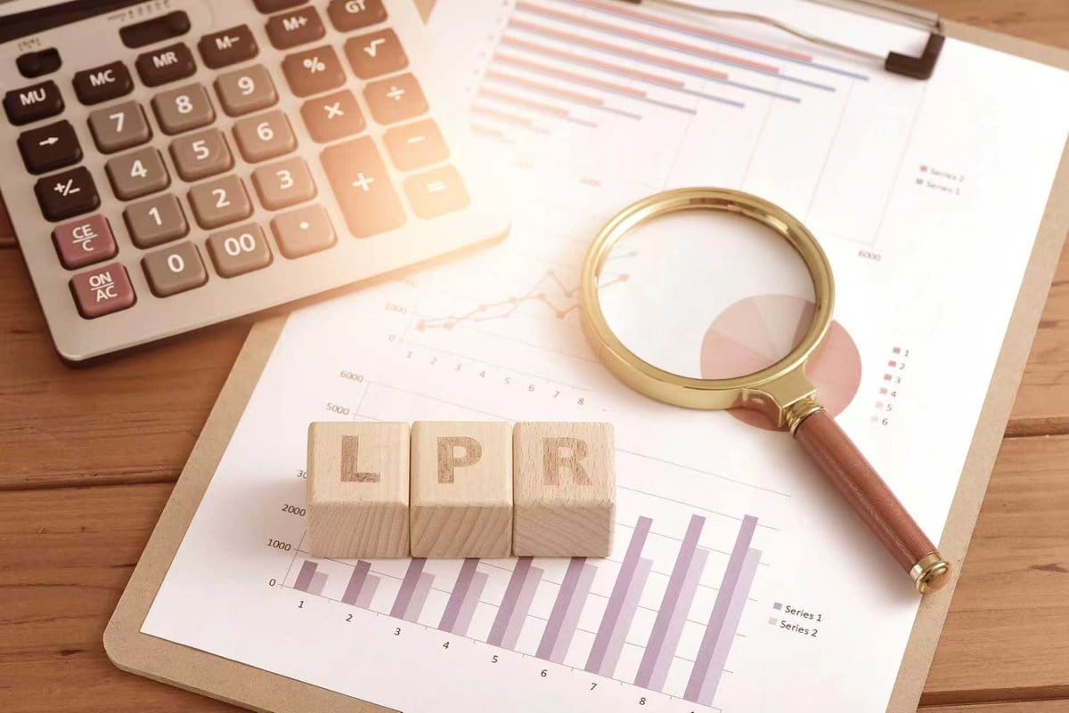 Wooden blocks spelling LPR on financial charts with calculator and magnifying glass.