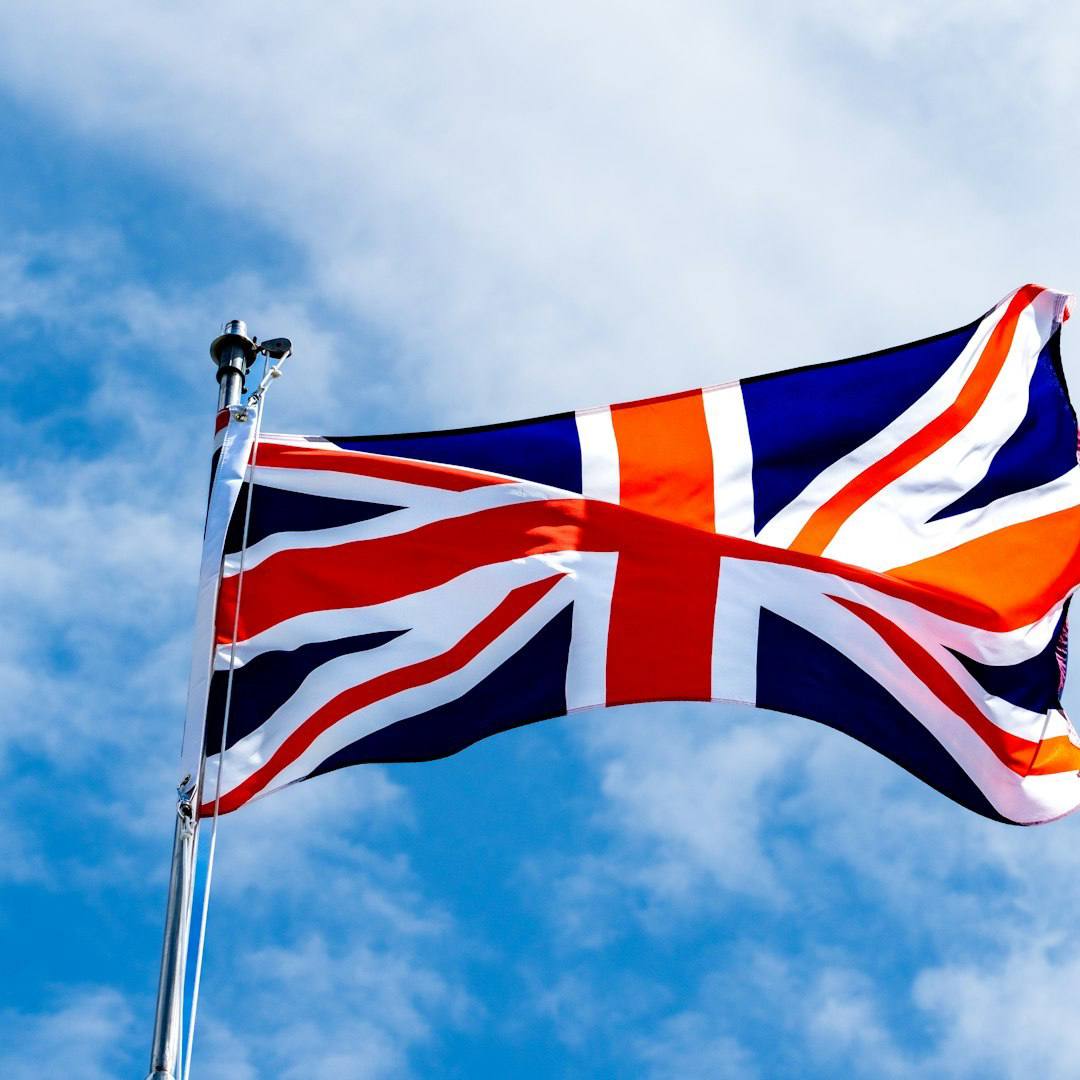 Union Jack flag waving on a flagpole against a blue sky.