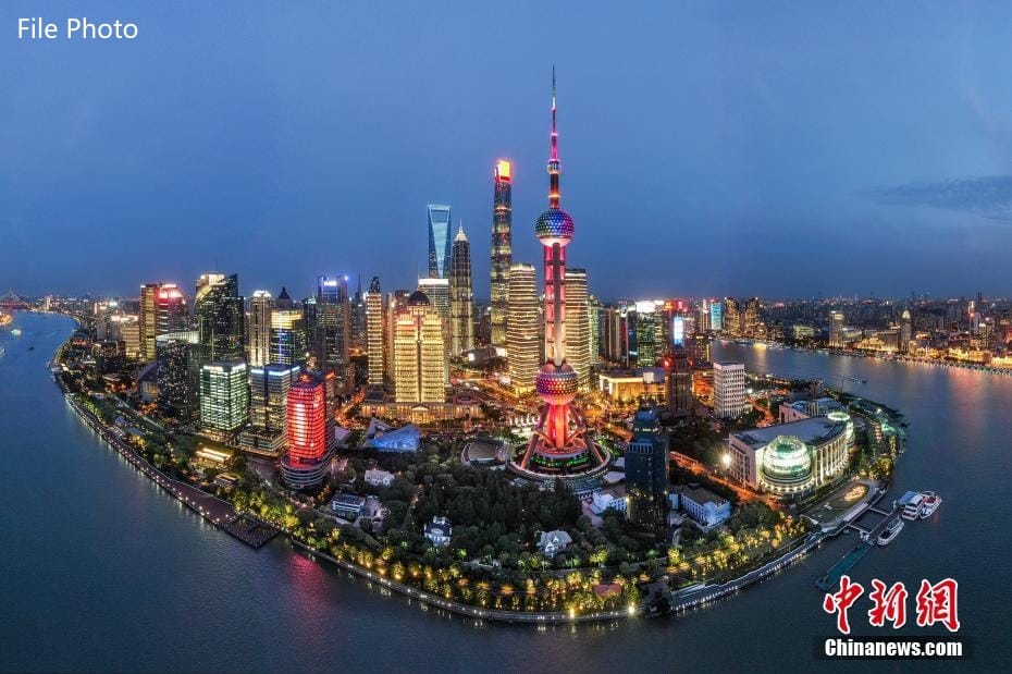 Nighttime aerial view of Shanghai skyline with Oriental Pearl Tower, illuminated skyscrapers, and river.