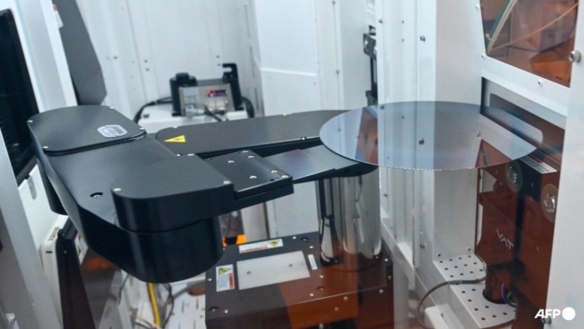 Robotic arm holding a circular silicon wafer inside semiconductor manufacturing equipment.