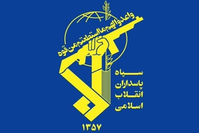 Yellow emblem on blue background showing a hand holding a rifle, a globe with a leaf, Arabic script, and the number 1357 at the bottom.