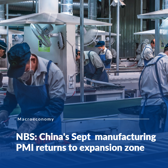 Factory workers in blue uniforms at an assembly line with overhead fans and industrial machinery.
