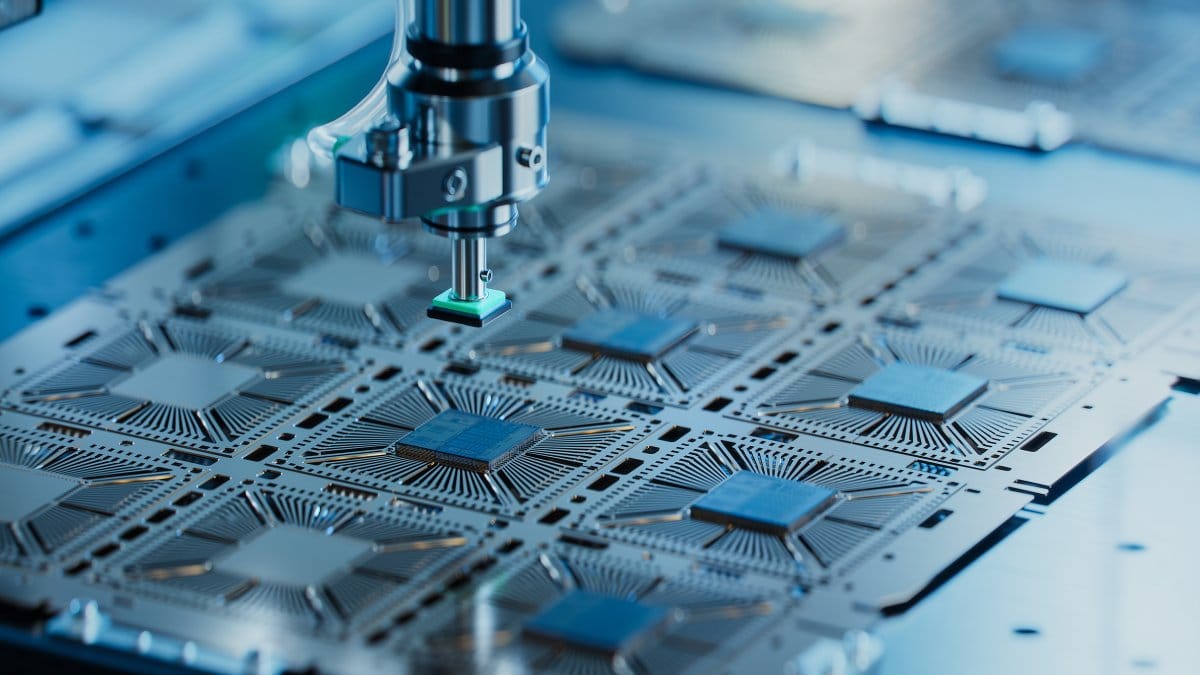 Robotic arm placing a microchip onto a metal leadframe of semiconductor packages in a factory.