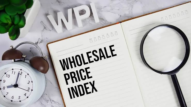 Open notebook labeled WHOLESALE PRICE INDEX, white WPI letters, analog clock, magnifying glass and small plant on a marble surface.