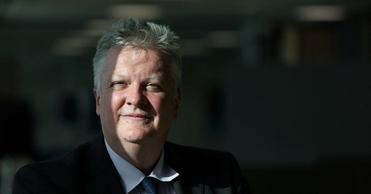 Head-and-shoulders portrait of a middle-aged man with short gray hair in a dark suit, white shirt and blue tie, facing the camera.