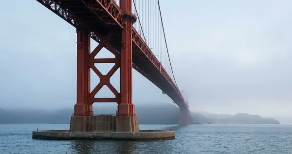 Massive pylons of a suspension bridge rising out of the water and supporting the towers of the Golden Gate Bridge, shrouded in fog above 