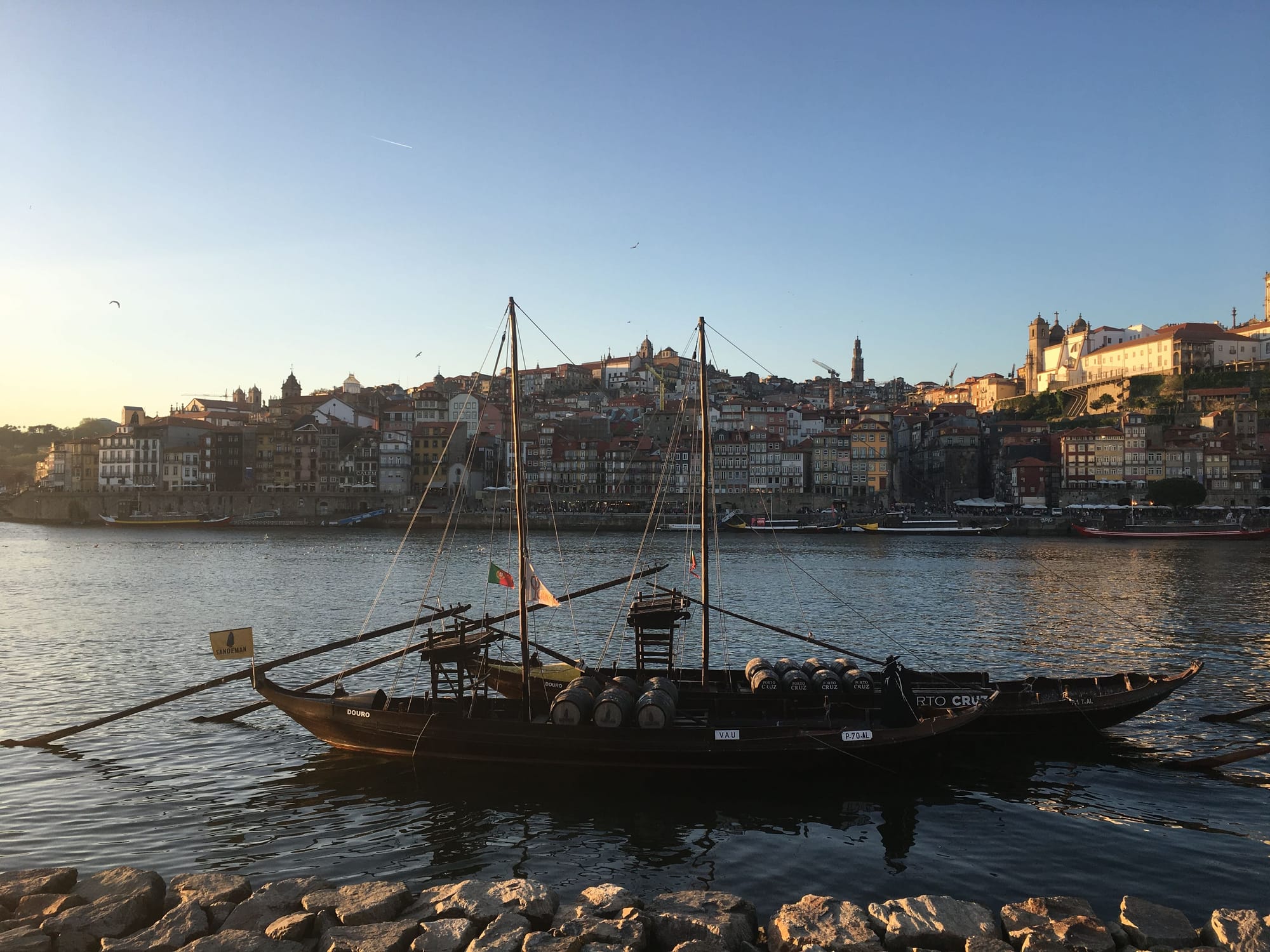 Two port boats on the side of Douro river across from scenic rows of buildings leading up the hills of Porto.