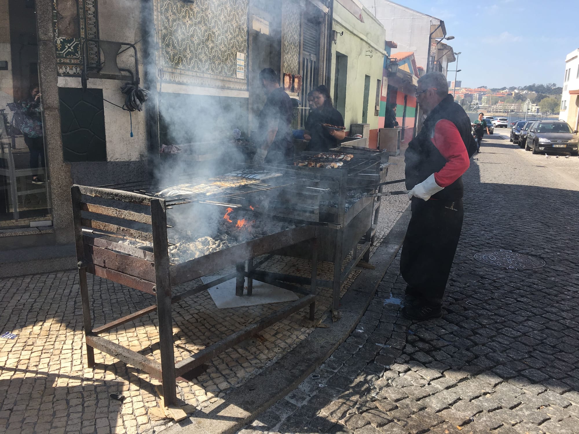 A chef stands next to multiple smoking charcoal grills cooking fish and meats for the restaurant in front of him.