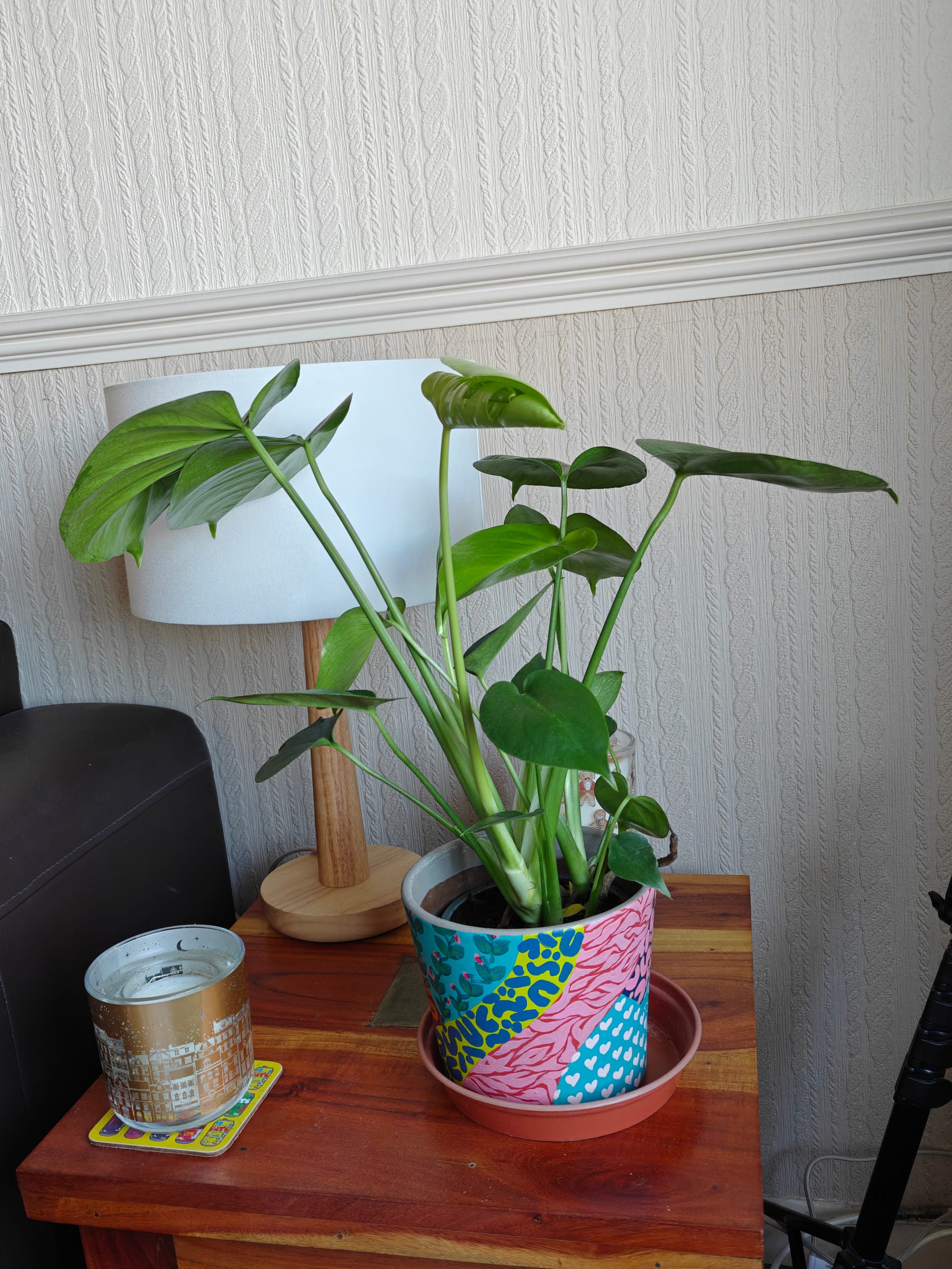a monstera plant in a colourful hand-painted pot on a wooden end table next to a lamp and a small Christmas candle