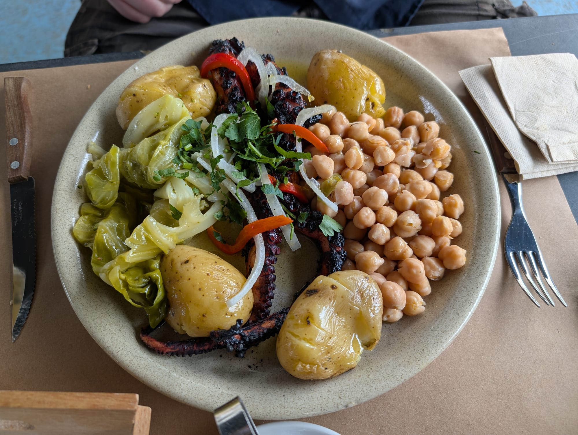 A plate of grilled octopus served with chickpeas, new potatoes, cabbage, peppers and herbs.