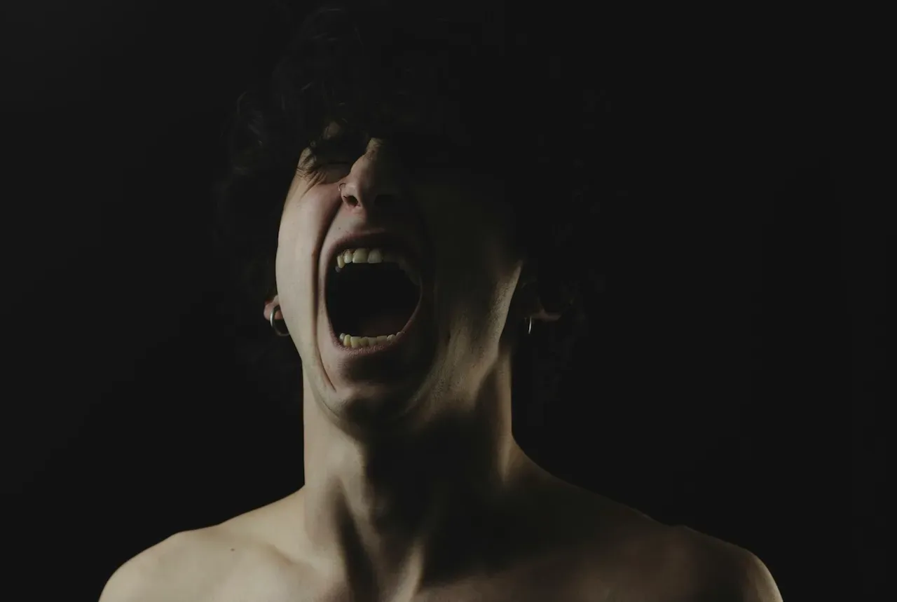 A dramatic photo of a young man screaming in the dark, with his face partially obscured.