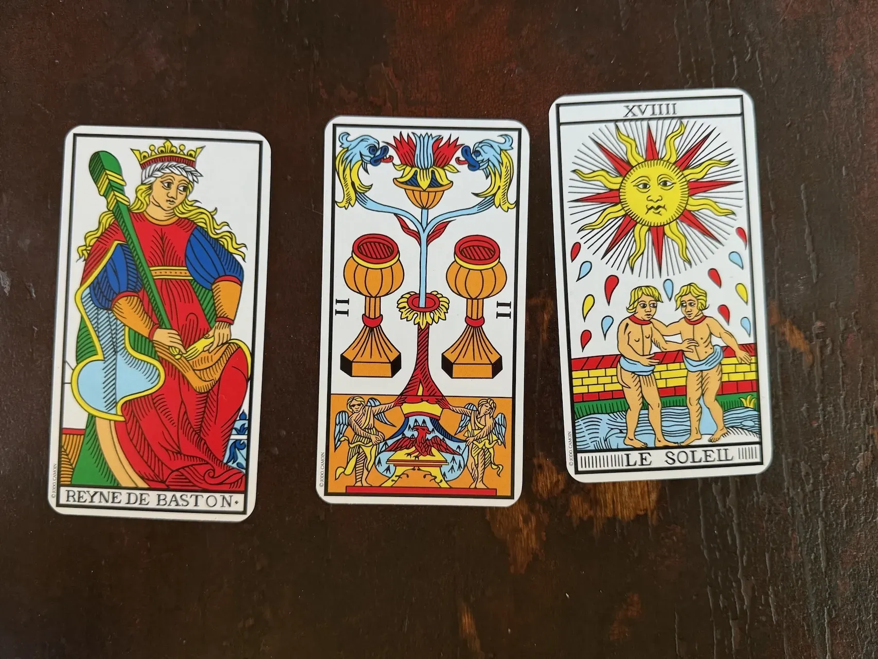 Three tarot cards: Queen of Wands, Two of Cups, The Sun