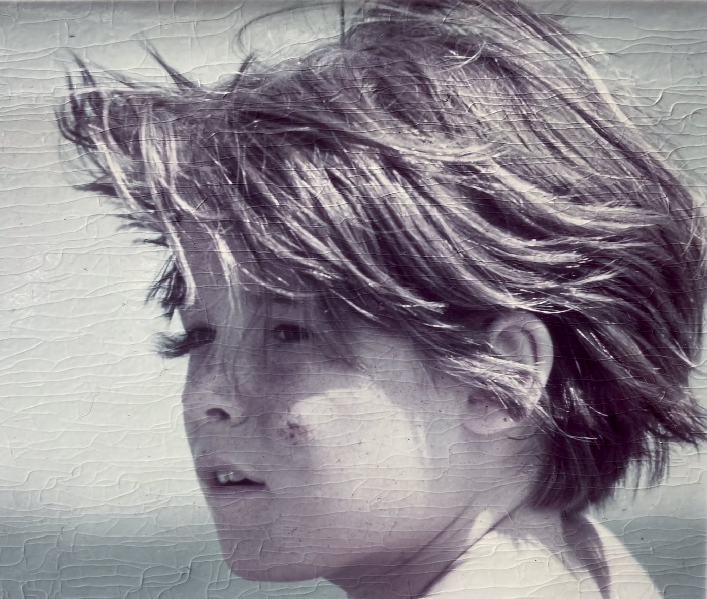 Close vintage photo of a young boy with light skin, freckles, and windswept hair. He has a calm and curious expression.