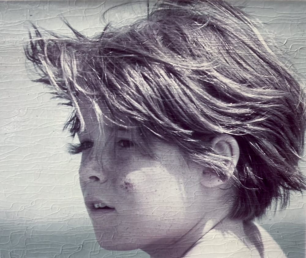 Close vintage photo of a young boy with light skin, freckles, and windswept hair. He has a calm and curious expression.